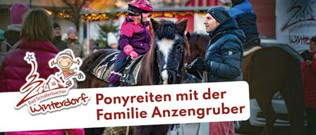 Ein Kind reitet auf einem Pferd, während ein Mann die Zügel hält. Das Kind trägt einen Helm und Handschuhe. Der Mann trägt eine Mütze und eine gefütterte Jacke. Das Pferd hat einen weißen Fleck auf dem Gesicht. Im Hintergrund befindet sich ein roter Stall.