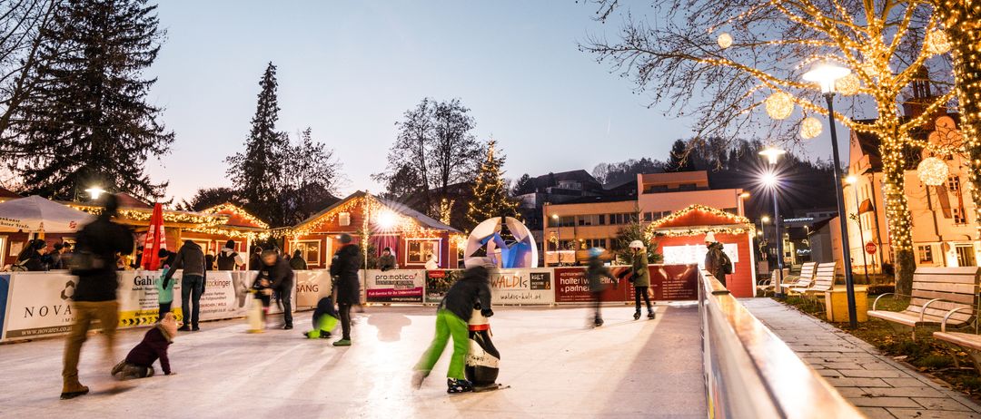 Ein Abend auf einer Eislaufbahn im Freien, umgeben von festlicher Dekoration, mit Schlittschuhläufern und Verkäufern in der Nähe.