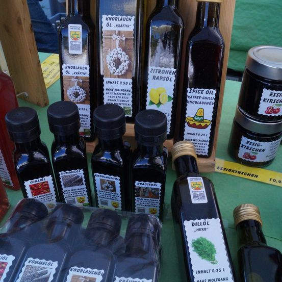 Verschiedene Flaschen mit aromatisierten Ölen sind auf einem grünen Tisch ausgestellt. Jede Flasche hat ein Etikett, das ihren Geschmack und ihre Zutaten angibt.