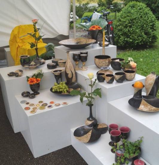 Ein Tisch zeigt verschiedene schwarze und weiße Keramikstücke, darunter Schalen, Tassen und Dekorationsartikel, neben Blumen und Pflanzen.