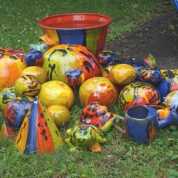 Eine bunte Sammlung von Keramikkunstwerken, darunter Frösche, Schildkröten und ein Eimer, verstreut auf dem Rasen.