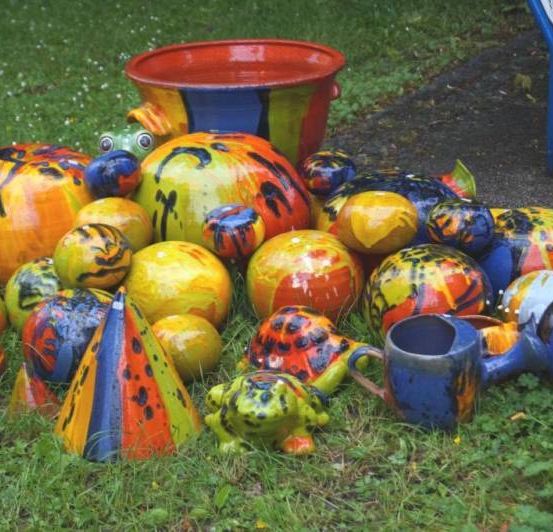 Eine bunte Sammlung von Keramikkunstwerken, darunter Frösche, Schildkröten und ein Eimer, verstreut auf dem Rasen.