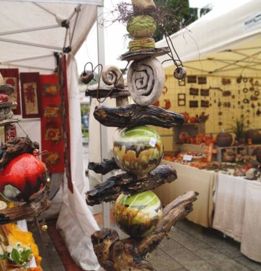 Ein Freiluftmarkt mit weißen Zelten und verschiedenen handgefertigten Dekorationen, darunter ein einzigartiges Stück aus Treibholz und Steinen, unter einem bewölkten Himmel.