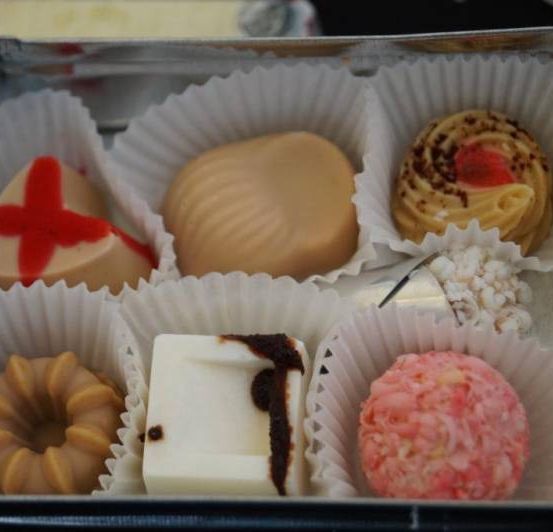 Ein Metallbehälter enthält verschiedene Pralinen in Papierbechern. Jede Praline hat eine einzigartige Form und Dekoration, mit Geschmacksrichtungen, die durch ihre Designs angedeutet werden.