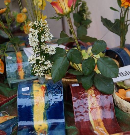 Dekorative Vasen mit Blumen, einschließlich Rosen und weißen Blumen, sind auf einem Tisch mit anderen Gegenständen angeordnet.