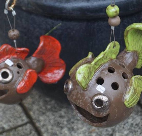 Zwei Keramikfische hängen an einem Metallobjekt. Ein Fisch hat eine rote Flosse und der andere eine grüne Flosse.