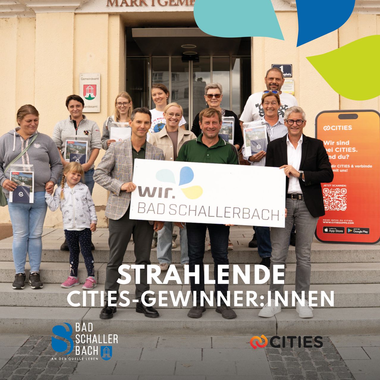 Eine Gruppe von Menschen steht vor einem Gebäude und hält ein Banner mit der Aufschrift 'Bad Schallerbach Strahlende Cities-Gewinner:innen'. Sie alle lächeln und scheinen für ein Foto zu posieren.