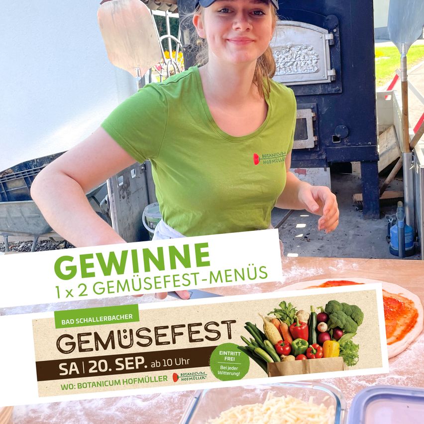 Eine Frau in einem grünen T-Shirt lächelt in die Kamera, während sie einen Pizzaschaufel in einer Bäckerei hält. Das Bild zeigt auch ein Schild für ein Gemüsefestival und eine Pizza auf einem Tisch.