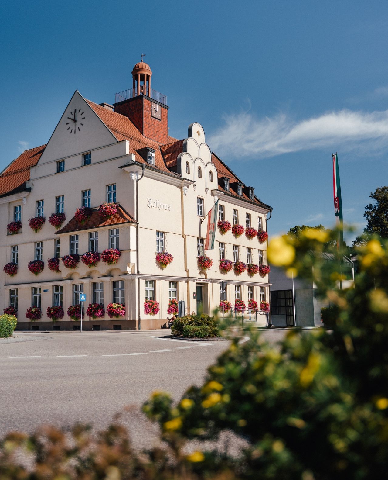 Ein großes Gebäude mit einem Glockenturm, rotem Dach und zahlreichen Blumenkästen. Das Gebäude heißt Rathaus. Eine Flagge steht auf der rechten Seite des Gebäudes.
