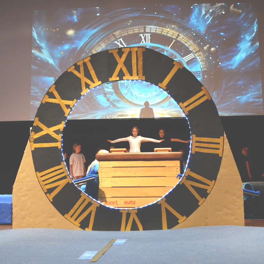 Eine riesige Uhr mit römischen Ziffern und einer Person im Inneren. Ein Bildschirm dahinter zeigt eine himmlische Szene.
