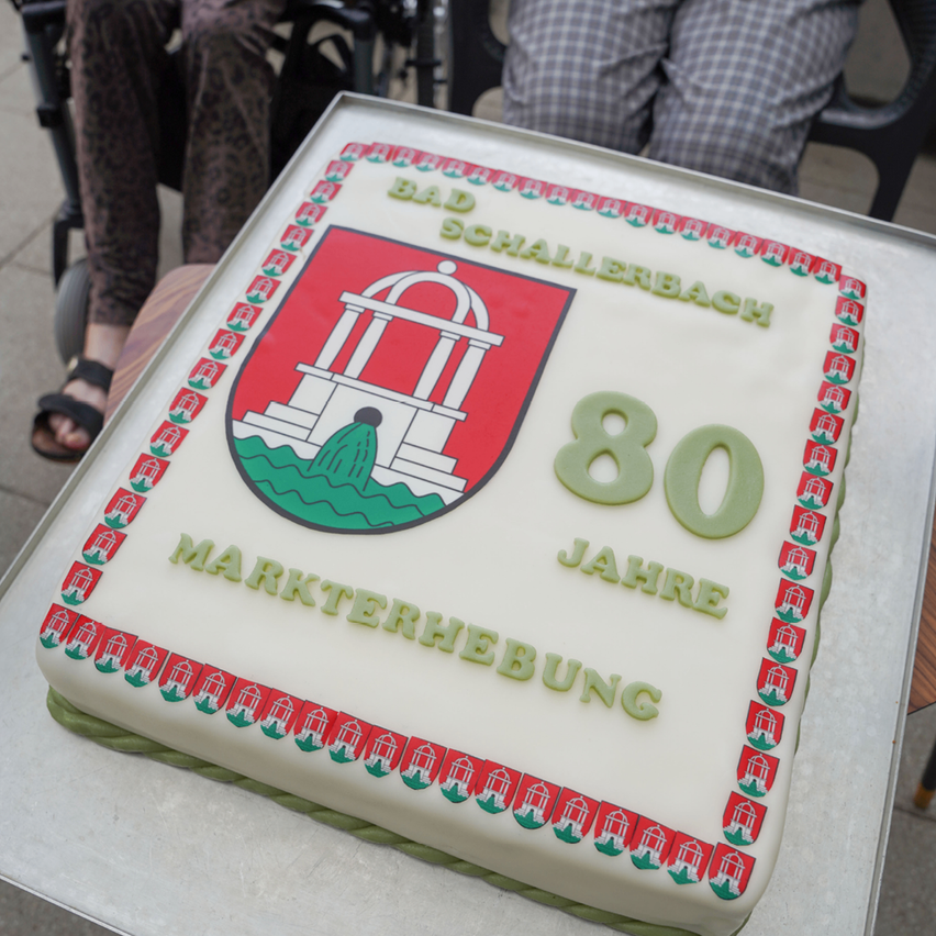 Ein Kuchen mit einem roten und grünen Emblem und den Worten 'Bad Schallerbach 80 Jahre Markterhebung' darauf geschrieben.