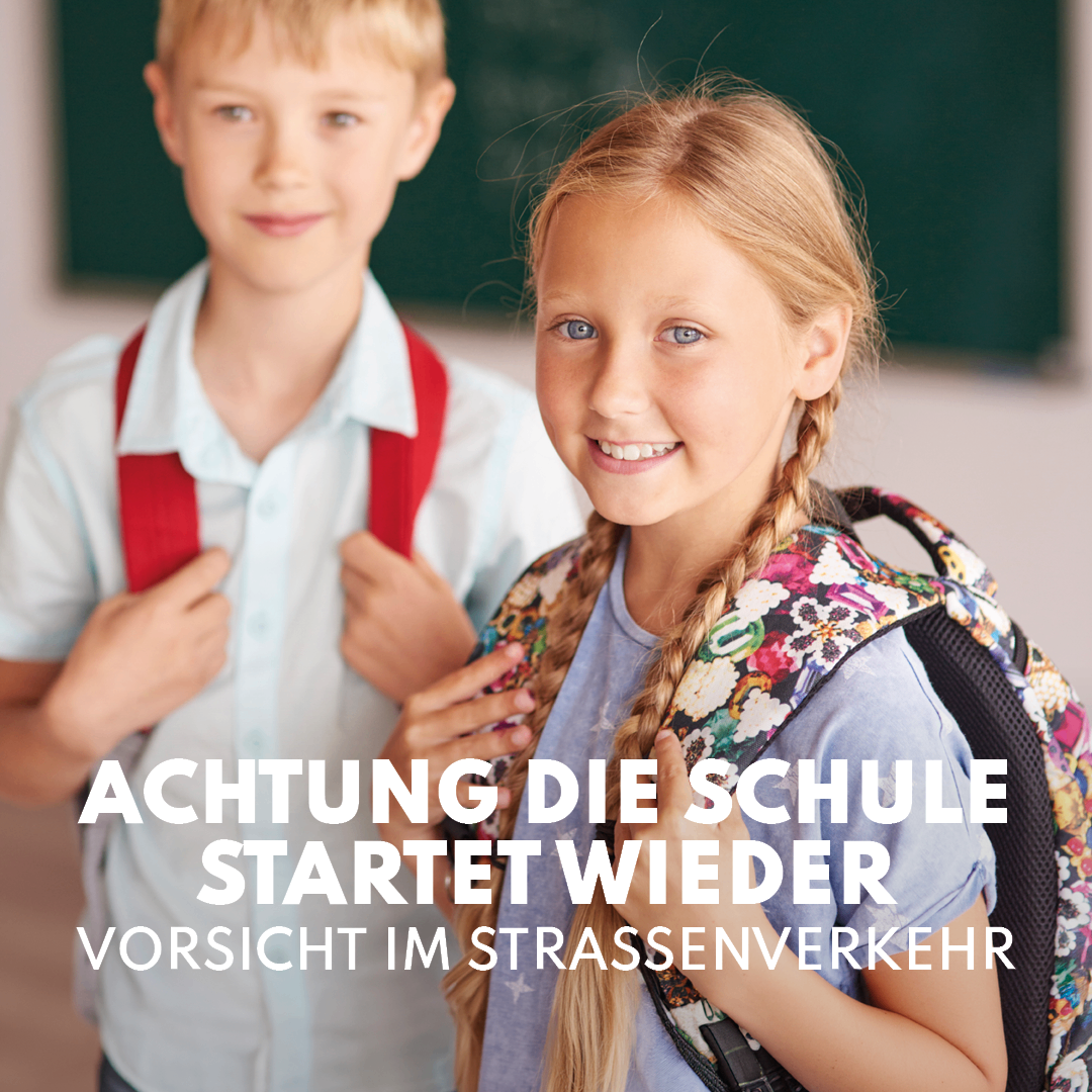 Two children, a boy and a girl, stand close together in a school corridor, smiling and carrying backpacks. The text overlay reads 'Attention, school starts again, caution in traffic.'