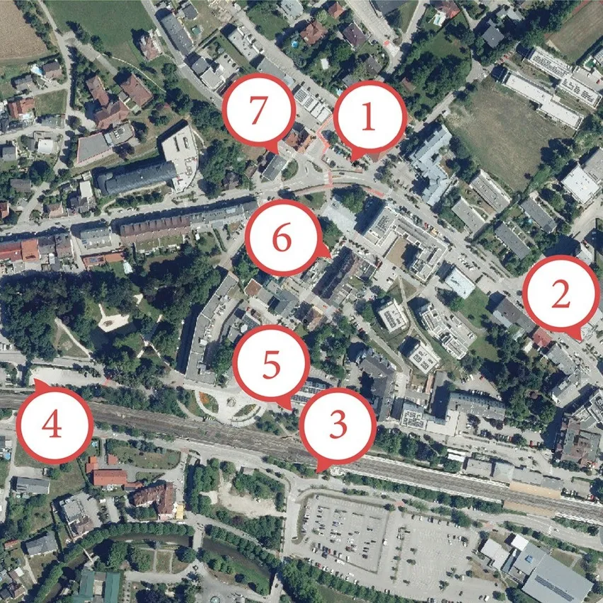 Ein Luftbild einer Stadt mit mehreren Gebäuden und einer Straße. Die Gebäude sind unterschiedlich groß und stilvoll, und einige von ihnen haben rote Kreise mit Nummern darauf.