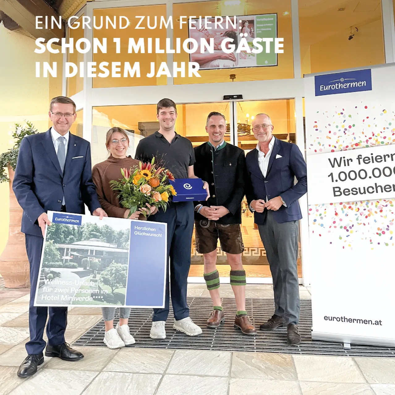Fünf Personen stehen vor einem Gebäude, halten ein großes Schild und einen Blumenstrauß. Das Schild lautet 'EIN GRUND ZUM FEIERN: SCHON 1 MILLION GÄSTE IN DIESEM JAHR'.