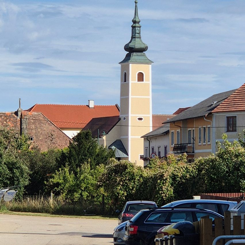 Eine Stadt mit einem Kirchturm und roten Dächern. Autos vor den Häusern geparkt.