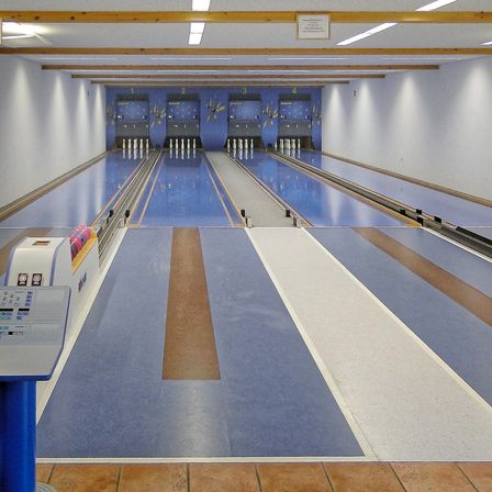Eine Bowlingbahn mit blauen Bahnen und braunen Holzakzenten. Die Bahnen sind derzeit leer.