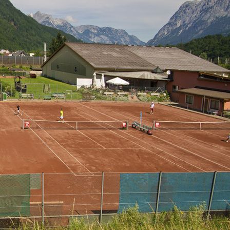 Tennisplätze im Freien sind eingerichtet, mit Spielern in verschiedenen Spielphasen, mit Bergen im Hintergrund.