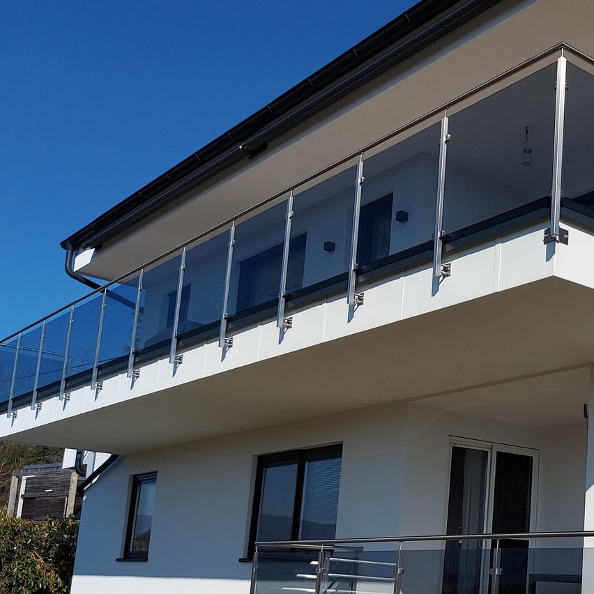 Ein modernes weißes Haus mit Glasgeländern und Fenstern unter einem klaren blauen Himmel.