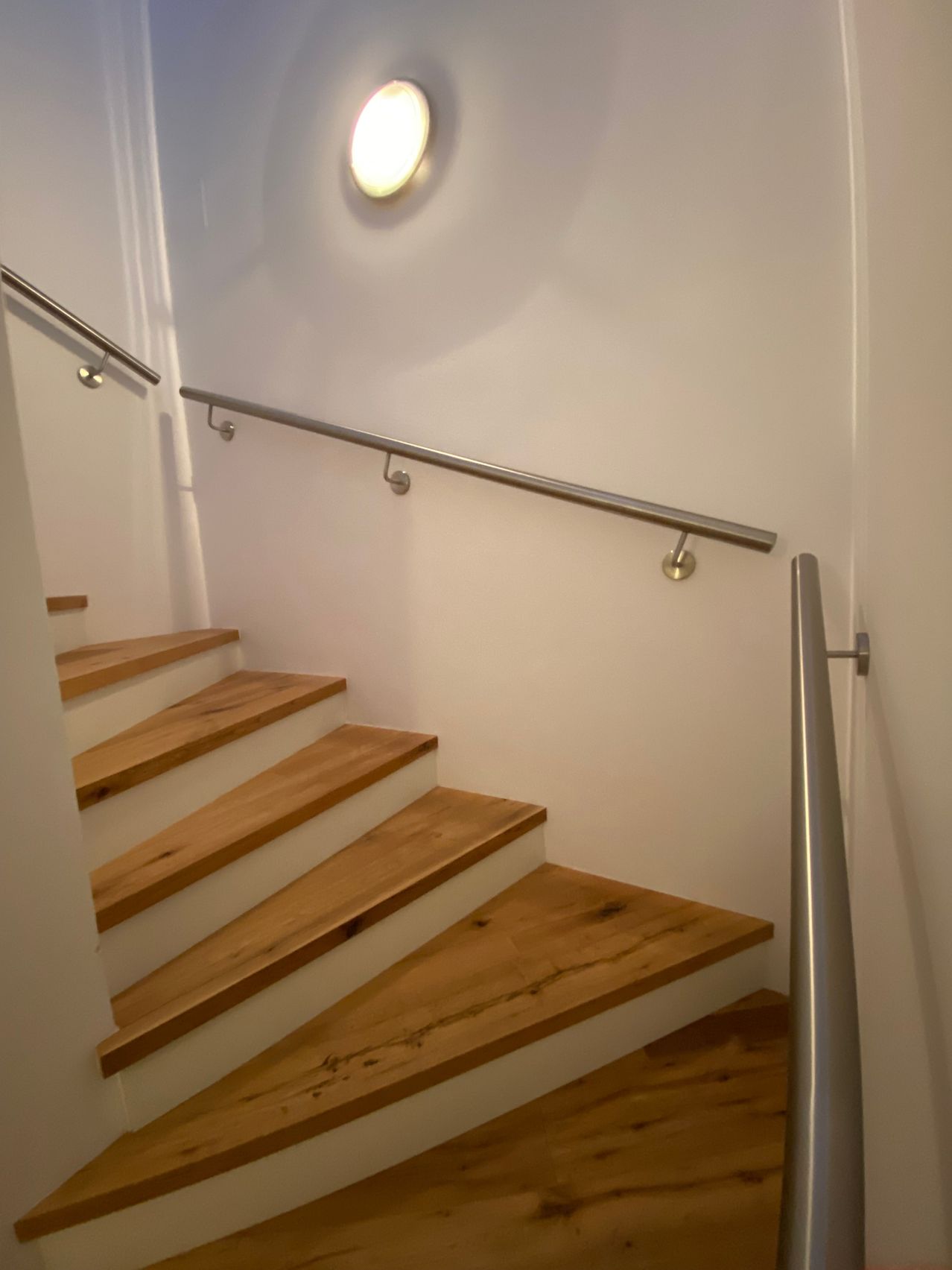 Eine Treppe mit Holzstufen und weißen Steigungen ist an einer weißen Wand befestigt. Metallgeländer sind an beiden Seiten der Treppe an der Wand befestigt.