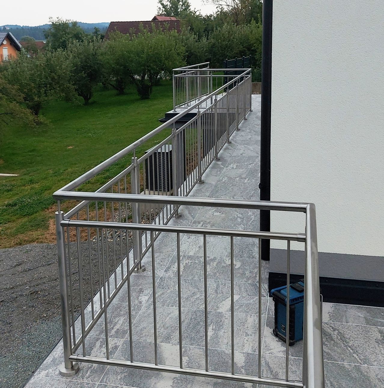 Ein Balkon mit einem modernen Geländer und Blick auf eine Rasenfläche und Bäume.