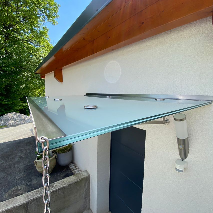 Ein modernes Hausaußendesign mit einer Glasüberdachung an der Wand, mit einer Tür und Pflanzen darunter auf Betonstufen.