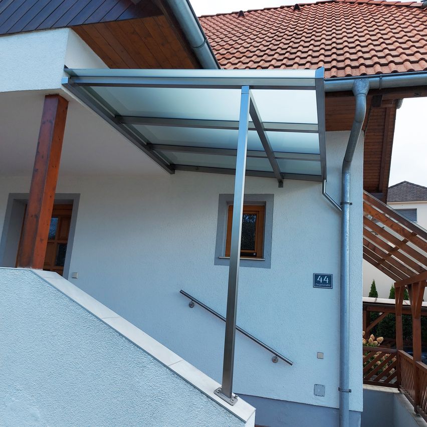 Ein Haus mit einem roten Dach und einem Glasvordach über dem Eingang mit der Nummer 44 an der Wand.