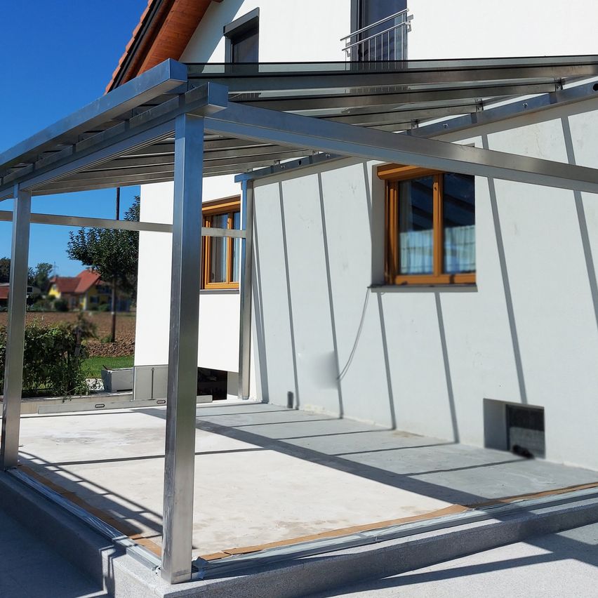 Vor einem modernen weißen Gebäude wurde eine neue Metall-Veranda errichtet, mit Glasfenstern und einem klaren blauen Himmel.