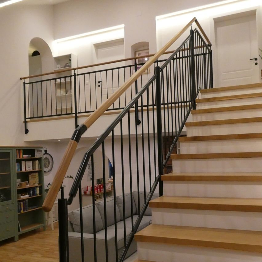 Ein Innenansicht eines modernen Hauses mit einer Holztreppe und einem Metallgeländer. Ein Sofa steht in der Nähe der Treppe.