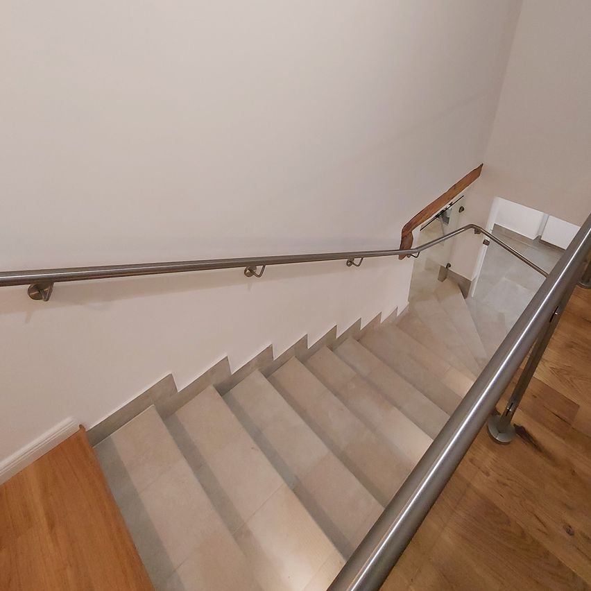 Eine weiße geflieste Treppe mit einem Metallgeländer steigt zu einer weißen Wand hinauf. Das Geländer ist mit Metallhalterungen befestigt.