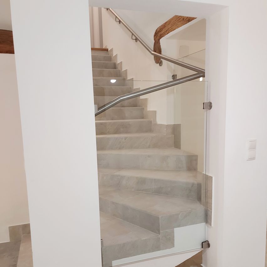 Eine moderne Treppe mit Marmorstufen und einem Glasgeländer, von einer Ecke aus gesehen, mit einem Holzbalken oben.