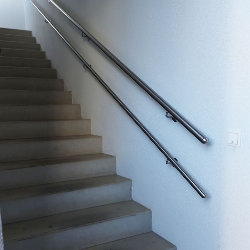 Eine Treppe mit mehreren Stufen und Metall-Handläufen, die an einer weißen Wand befestigt sind. Die Treppe ist aus Beton mit grauen Stufen.