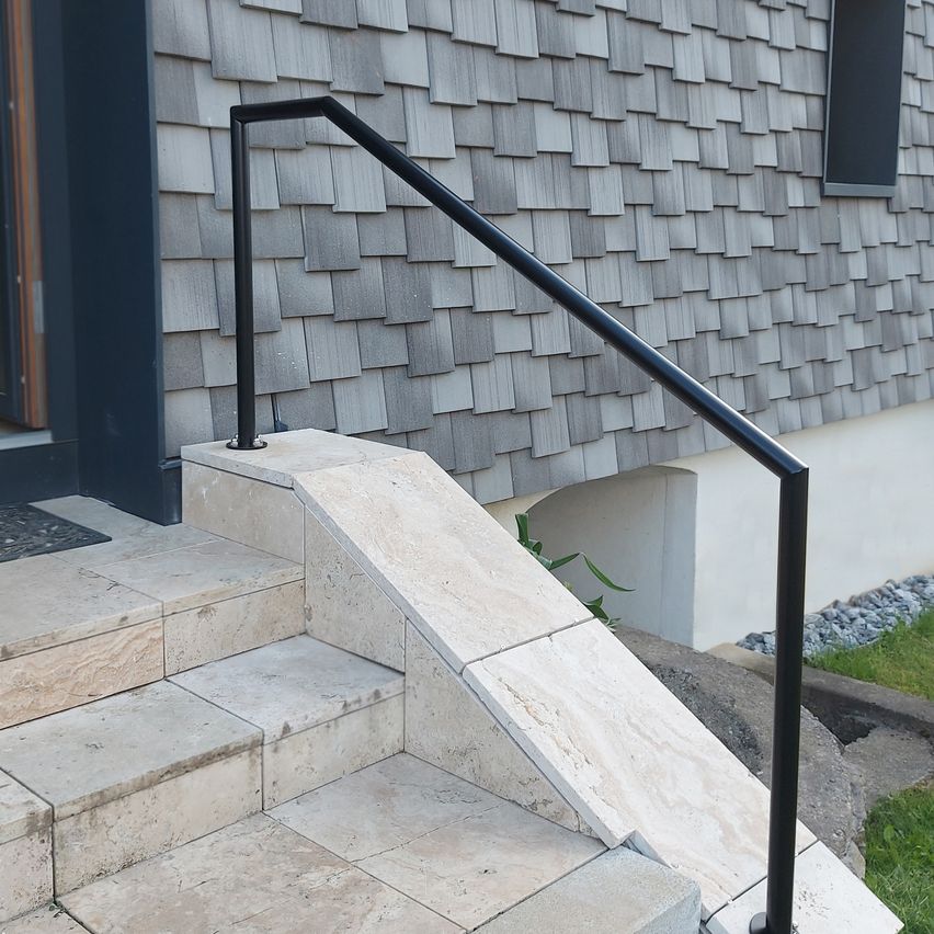 A modern house with a black handrail on the steps leading to the entrance.