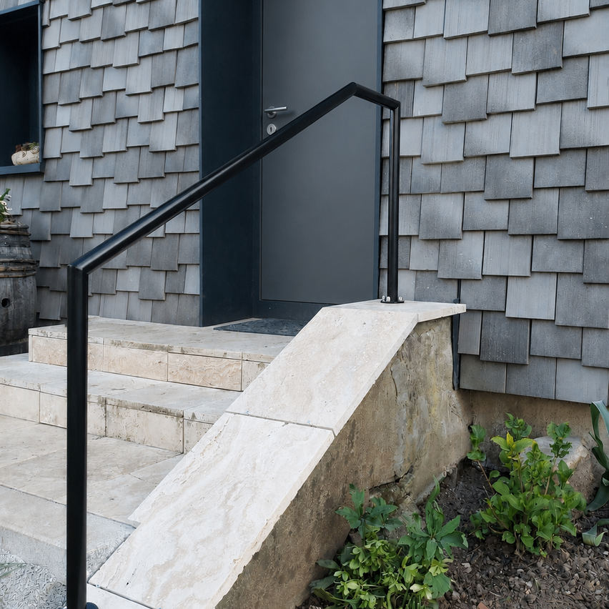 A modern house exterior with a black railing on the steps leading to a gray door. The house has a shingled roof and a small window with a plant inside.