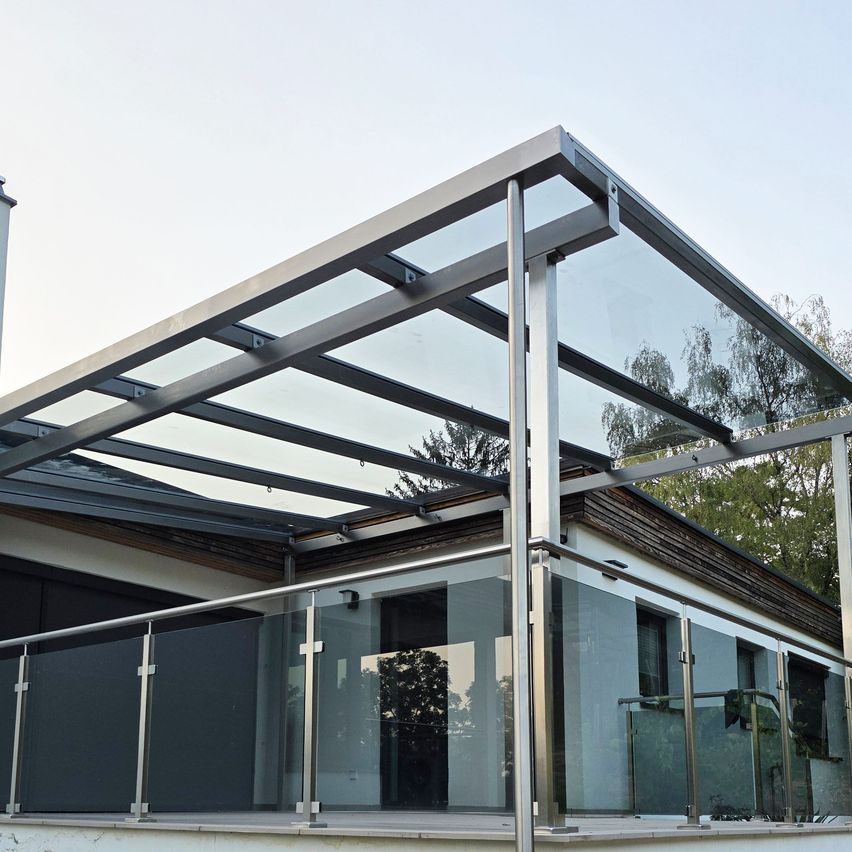 A modern house with a glass-roofed balcony, featuring a metal frame and glass panels, surrounded by trees.