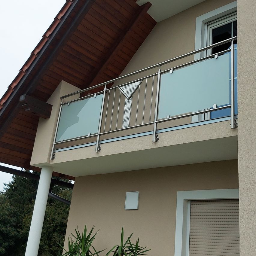 A modern house exterior with a balcony featuring a glass railing and a white shutter below.