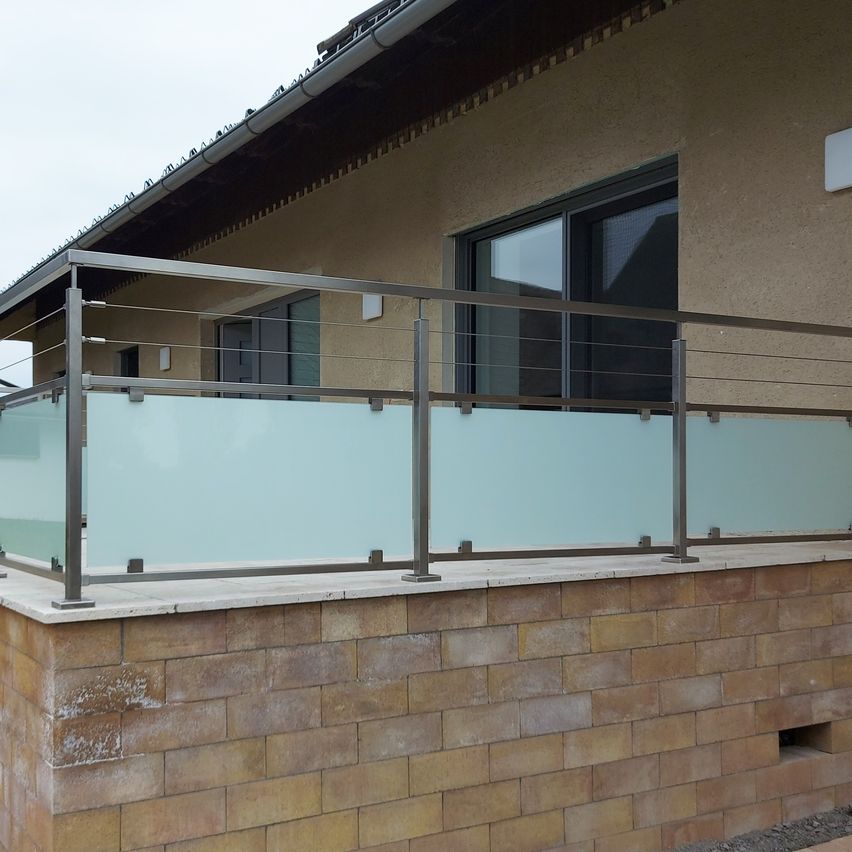 Ein modernes Haus mit Balkon hat Glasgeländer und eine Ziegelmauer. Der Himmel ist bedeckt.