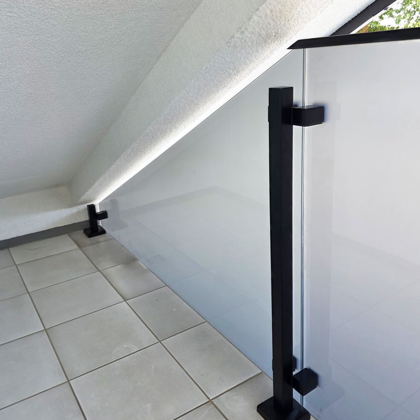 A close-up view of a modern, white glass wall with a black metal railing, set against a white ceiling and tiled floor.
