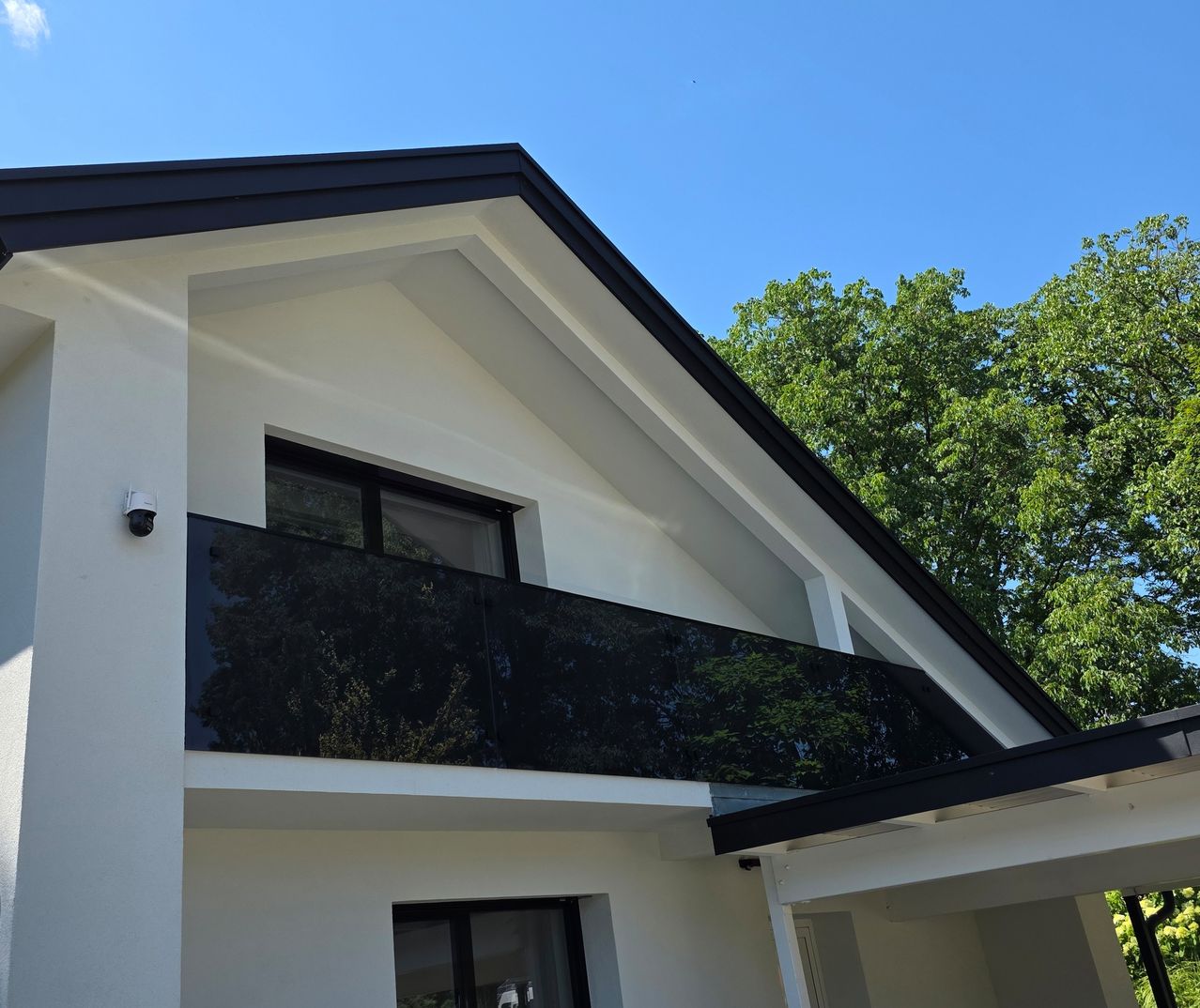 A modern white house with a black-framed balcony and glass railings under a clear blue sky.