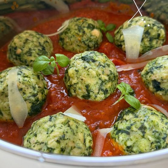 Eine Nahaufnahme eines Tellers mit Spinat- und Käsebällchen in Tomatensauce, garniert mit Basilikumblättern und Parmesan.