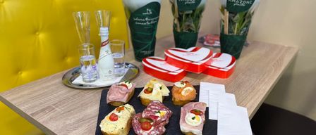 A table set with various foods, drinks, and flowers. A plate with sandwiches and eggs, with a bottle of wine, glasses, and flowers in vases.