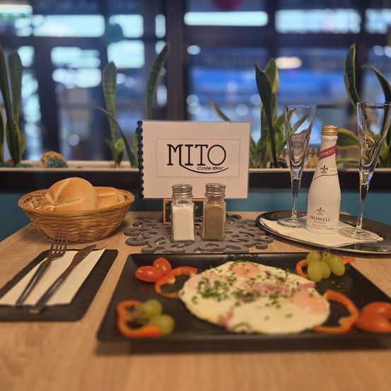 Ein Tisch für das Frühstück gedeckt mit Brot, Eiern, Tomaten und Trauben, begleitet von Salz- und Pfefferstreuern und einer Flasche Wein.