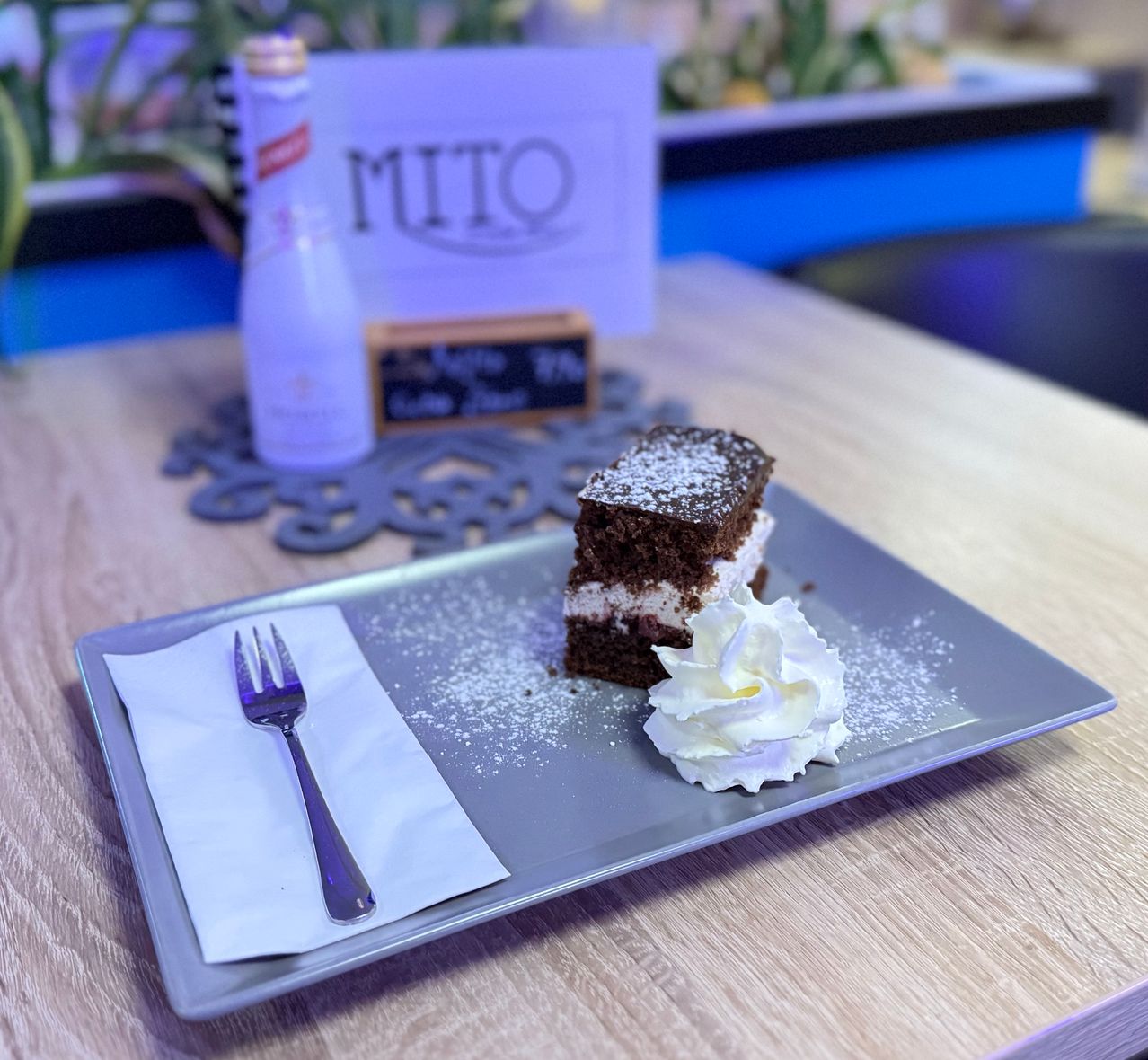 Ein Stück Schokoladenkuchen mit Schlagsahne auf einem Teller mit einer Gabel, begleitet von einer Flasche und einer Speisekarte.