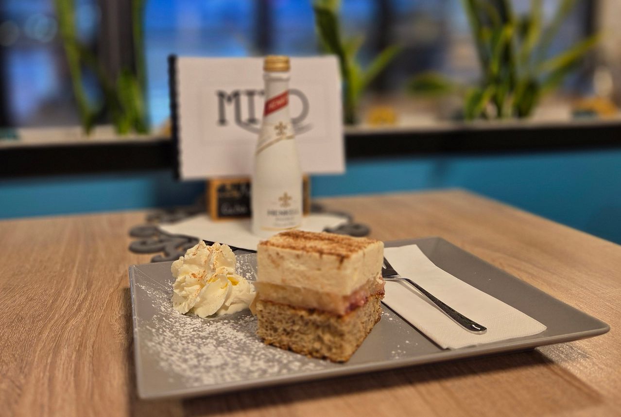 A dessert on a plate with whipped cream and a bottle of wine in the background.