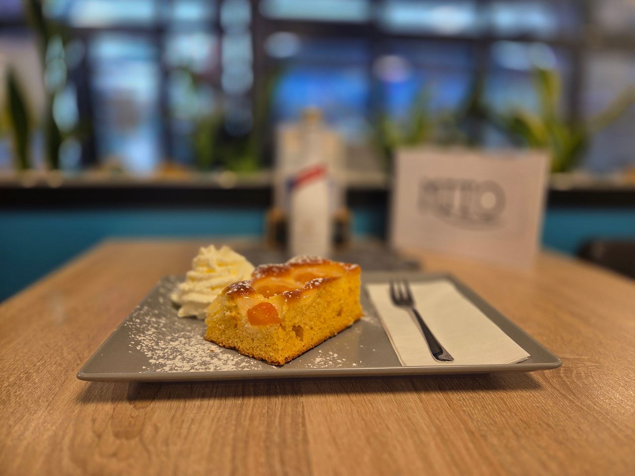 A slice of cake with a dollop of whipped cream and a fork on a plate sits on a wooden table.