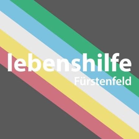 Ein bunter gestreifter Hintergrund mit dem Text 'lebenshilfe Furstenfeld' in weißer Schrift. Die Streifen sind rot, gelb, grün, blau und weiß.