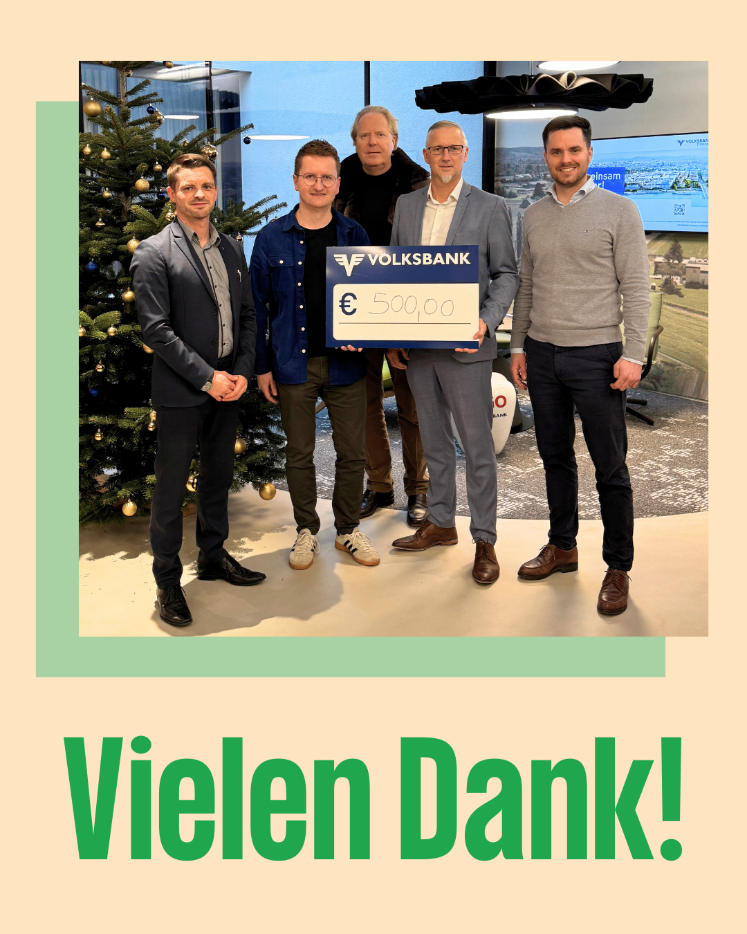 Fünf Männer stehen vor einem geschmückten Weihnachtsbaum. Ein Mann hält einen Scheck über 500 Euro von der Volksbank.