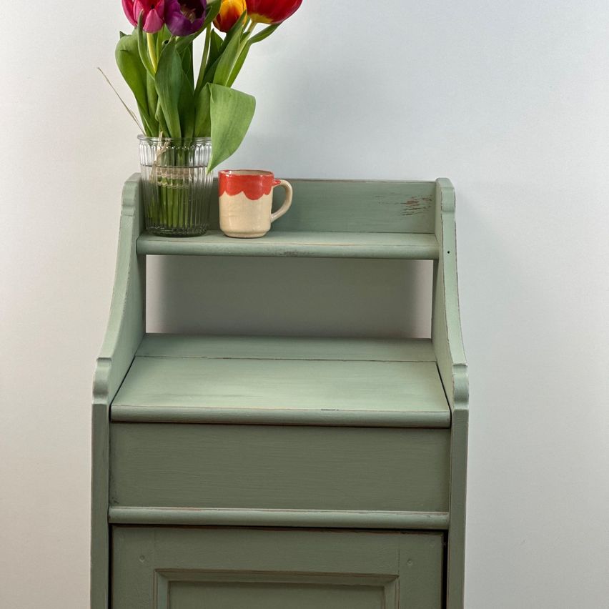 A green wooden shelf against a white wall, holding a vase of colorful tulips and a red and white coffee mug.