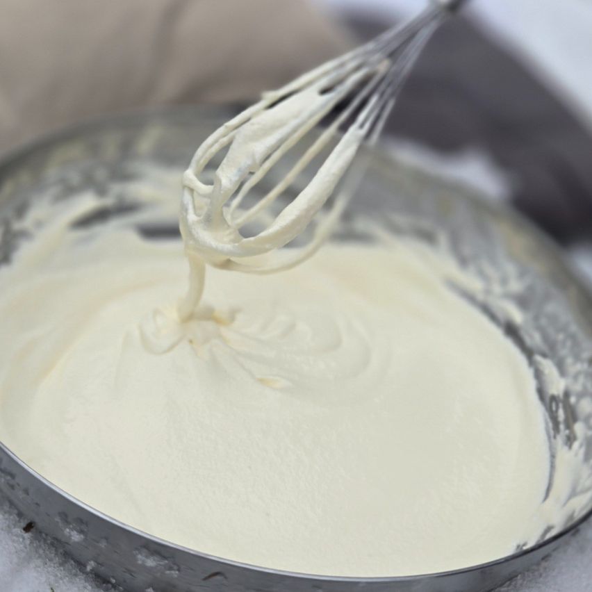 A whisk is being used to mix thick, creamy white batter in a bowl, ready for baking.