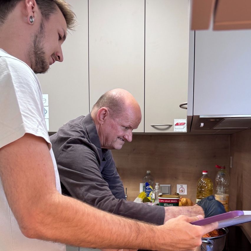 Zwei Männer in einer Küche, einer hält einen lila Teller und der andere lächelt und schaut ihn an.
