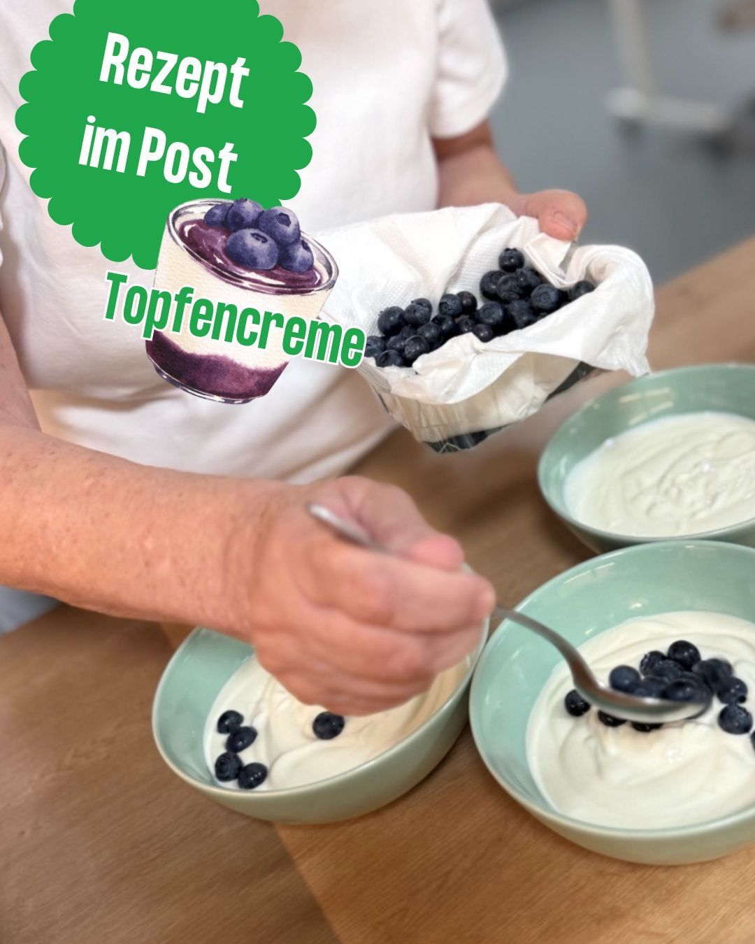 Eine Person bereitet ein Dessert mit Blaubeeren und Joghurt in einer Schüssel zu, wobei sie einen Löffel benutzt. Das Bild hat eine grüne Überlagerung mit Text.